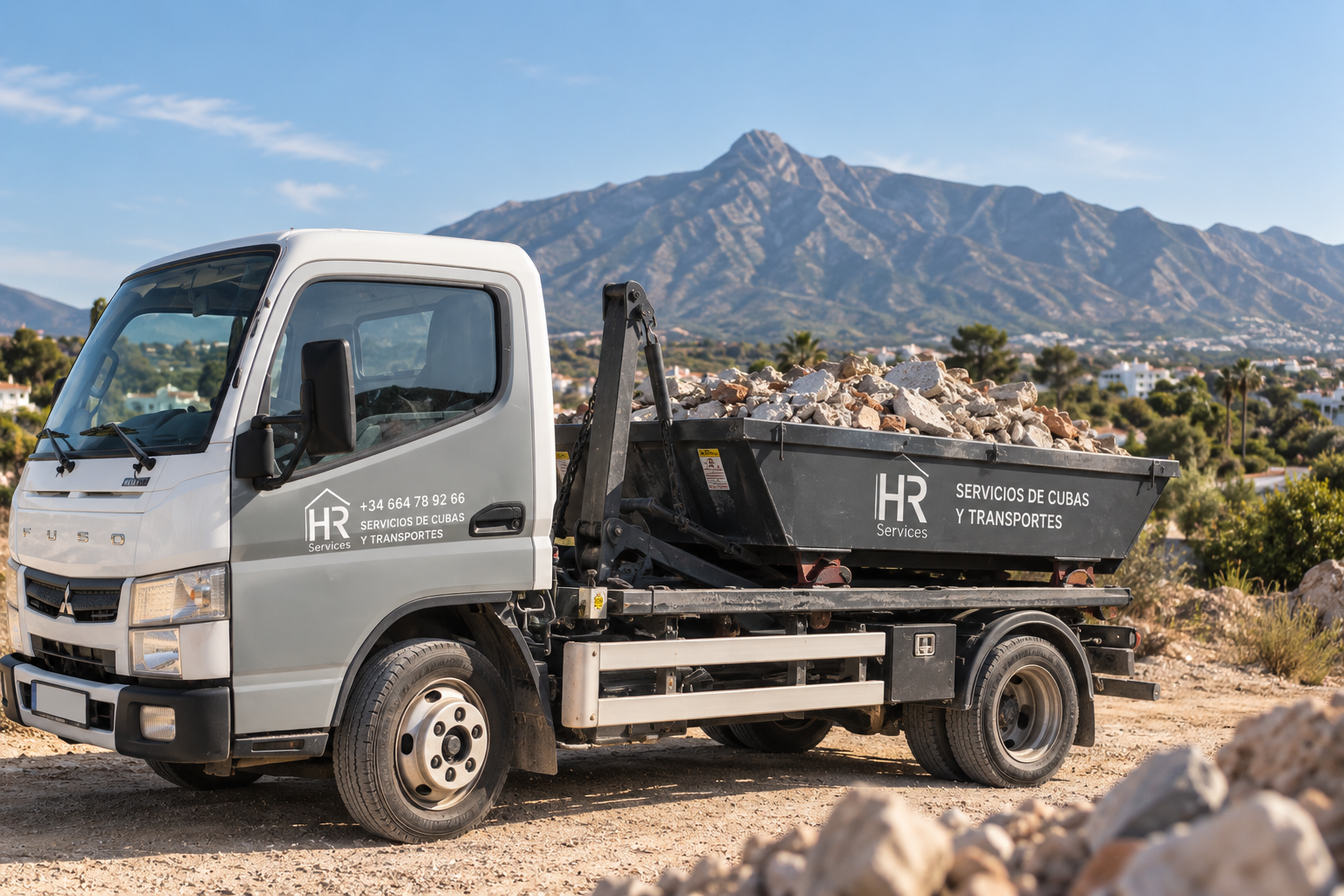 Camión HR Services con una cuba de escombros y La Concha al fondo